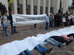 Возле Рады собрались активисты, требующие медреформы. Люди лежат, накрытые белым полотном, словно трупы